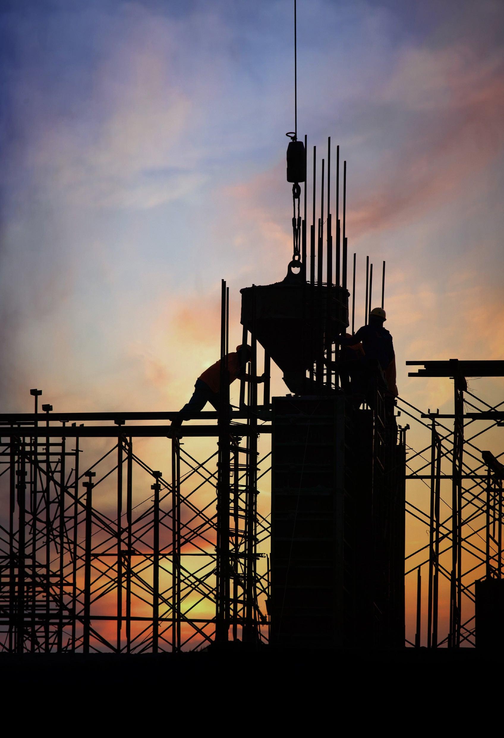 Construction crew guiding a concrete bucket onto a reinforced column at sunset