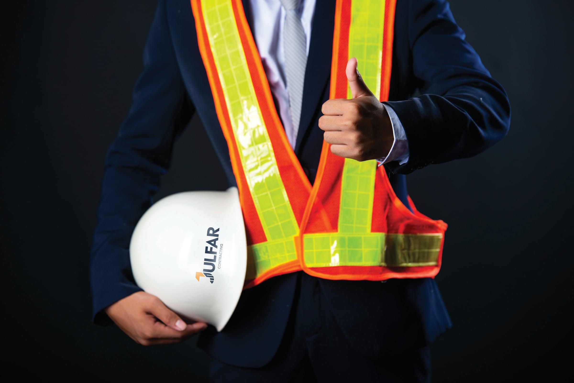 Site manager in a high-visibility vest holding a Julfar safety helmet